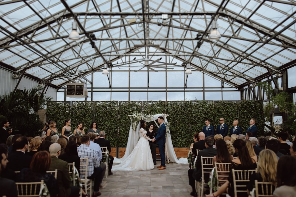 A wedding couple is getting married in a greenhouse at the Aquatopia Water Garden Conservatory, one of the wedding venues Ottawa offers.