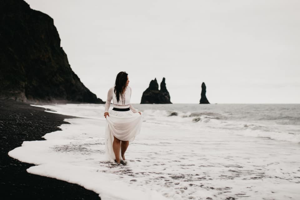 A bride is walking along the black sand beach in Iceland.
