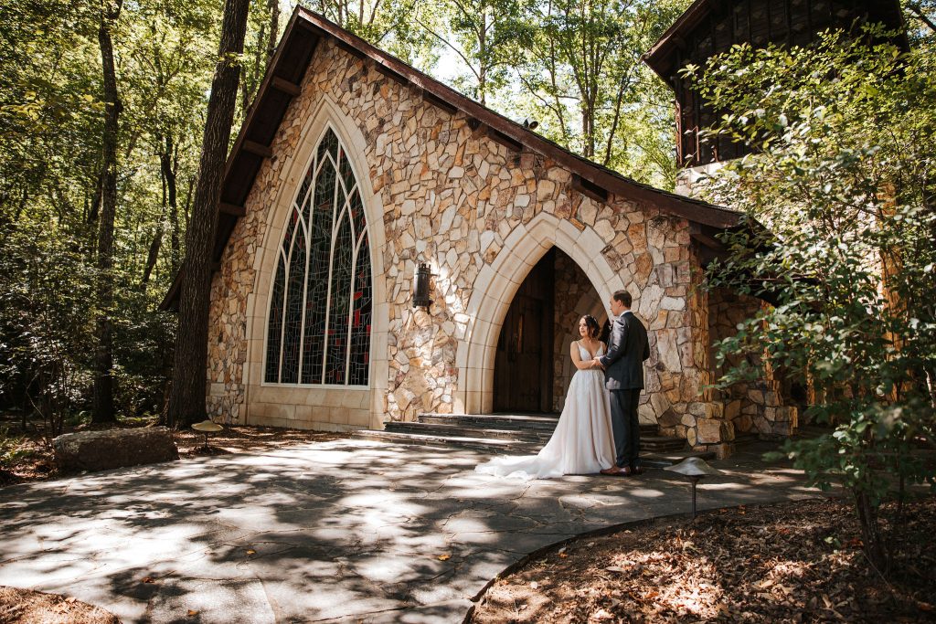 A wedding couple is standing in front of the Ida Cason Memorial Chapel at Callaway Gardens.