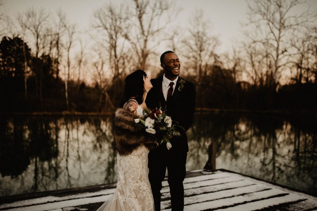 A wedding couple is laughing and standing on a dock next to a lake at Hopes Way Gathering Venue, one of the wedding venues Cincinnati has.