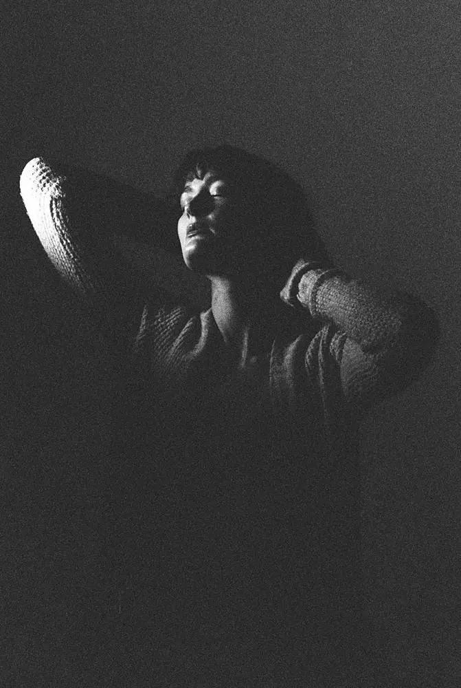 Moody black-and-white portrait of a woman: A black-and-white image of a woman with her hands behind her head, softly illuminated in low light. She has a serene expression with her eyes closed, creating a dramatic contrast against the dark background.