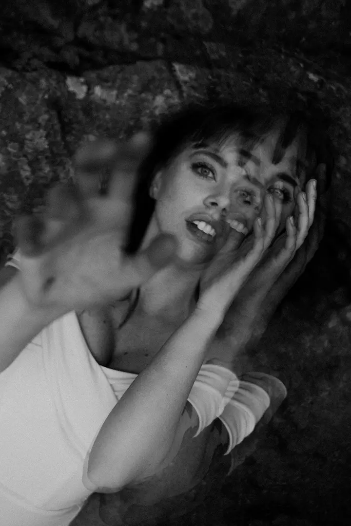 Double-exposure portrait of a woman reaching out: A black-and-white, double-exposure image of a woman lying down, with one hand reaching toward the camera. Her face is shown in overlapping layers, creating a dreamlike, surreal effect against a textured background.