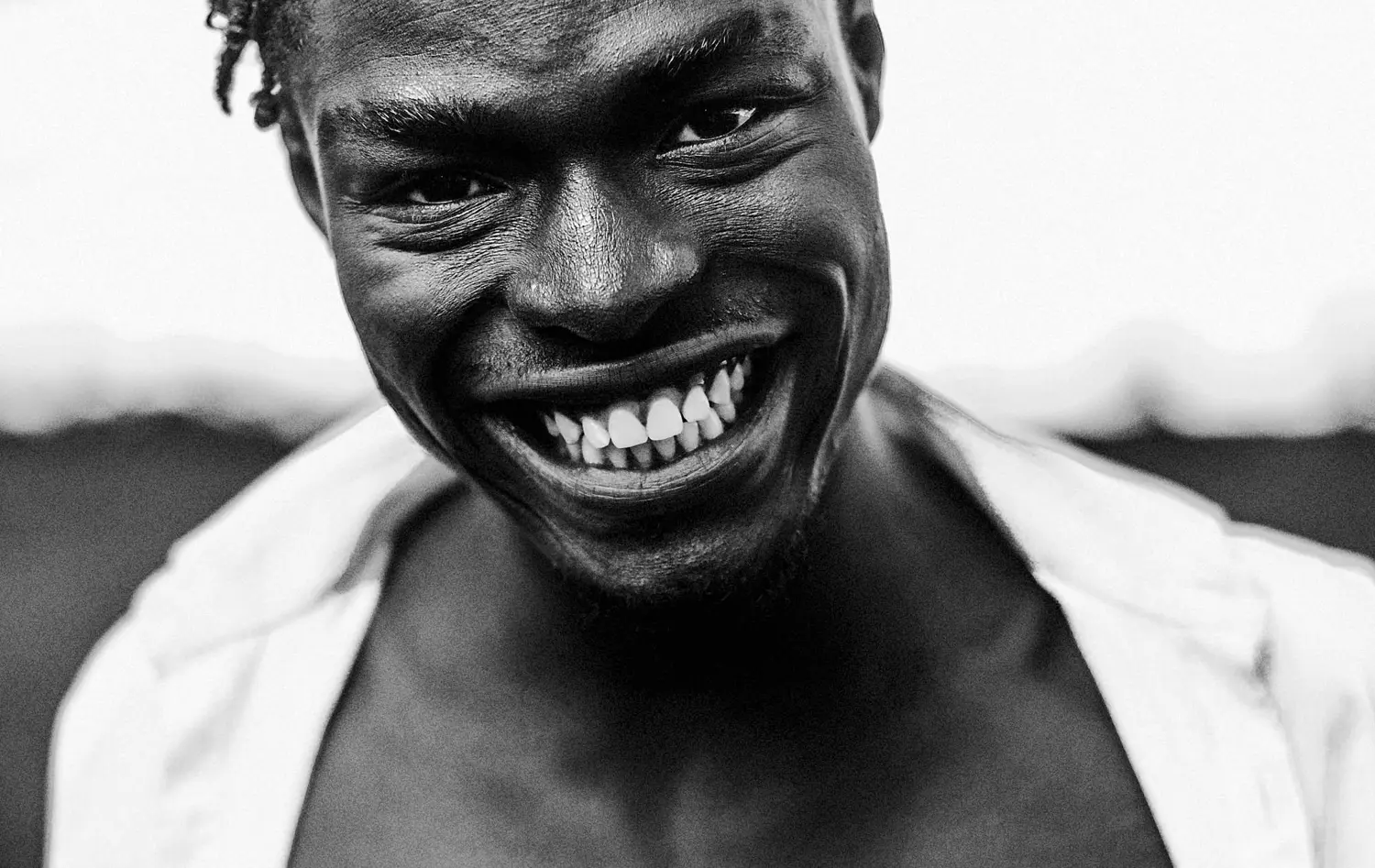 A high-contrast, black-and-white close-up of a man with a wide, joyful smile, showcasing his expressive features and dimples. This shot highlights creative portrait photography ideas by focusing on raw emotions, facial textures, and using black-and-white contrast to enhance the subject’s natural charisma.